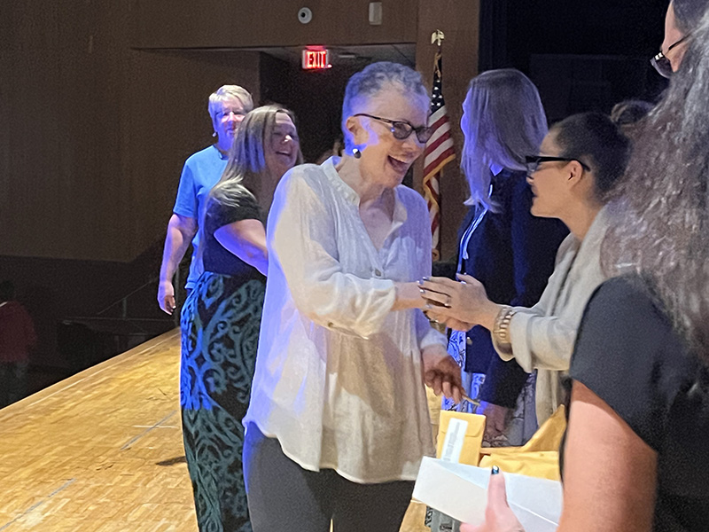 A woman wearing glasses shakes hands with a woman on the stage.