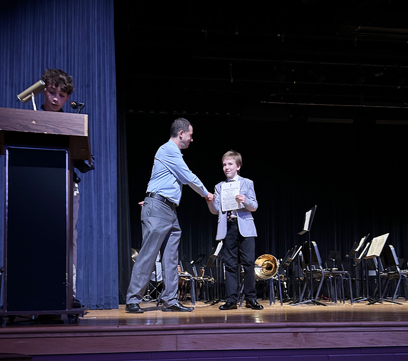 A middle school student shakes hands with a man on a stage.