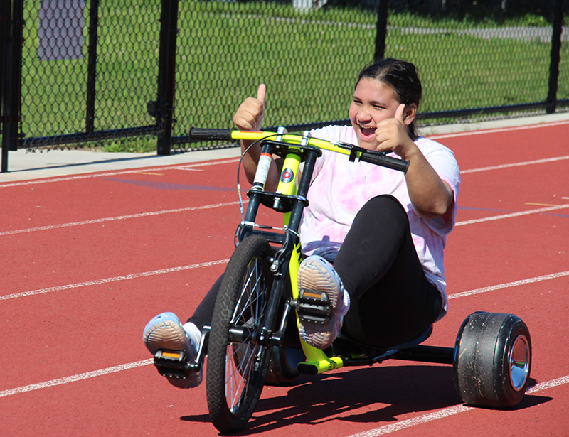 A high school girl sitting on a trike smiling and giving two thumbs up.