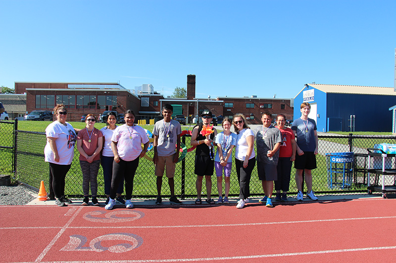 Seven high school students and four adults stand together smiling.