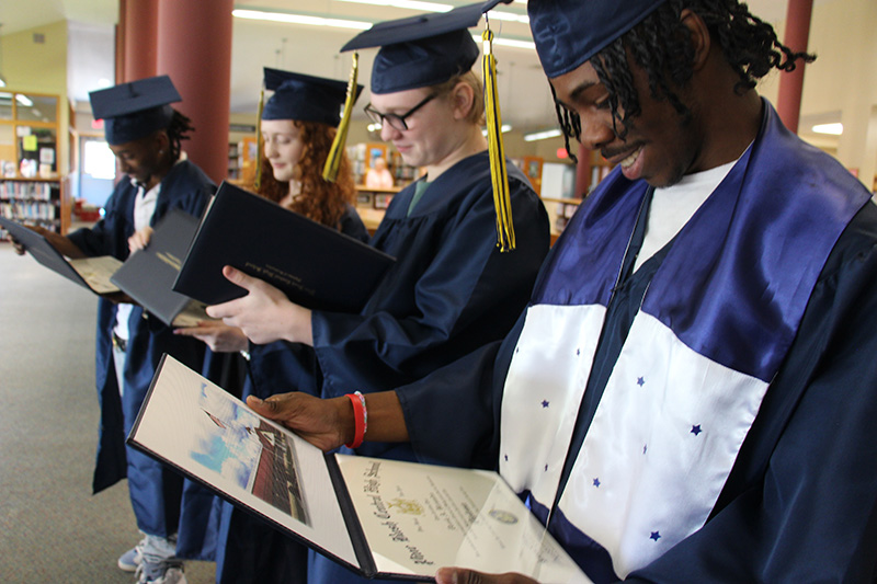 Four high school graduates wearing blue caps and gowns smile as they open their diplomas.