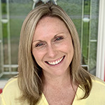 A woman with shoulder-length blonde hair smiles. She is wearing a yellow blouse.