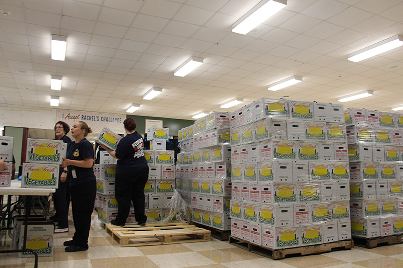 Stacks of boxes that say Fresh Produce are on crates and there are women working handing out the boxes.