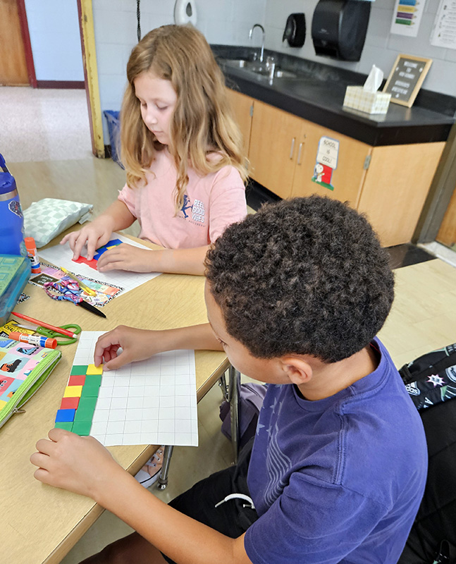 Two fourth-grade students use multi-colored tiles to create graphs.