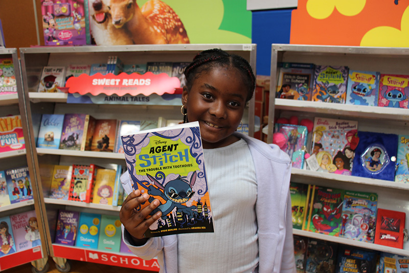 A girl holds up a book she is buying at a book fair. She is smiling.