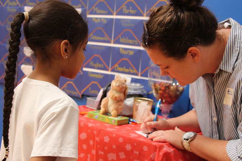 A girl watches as a woman writes on a piece of paper.