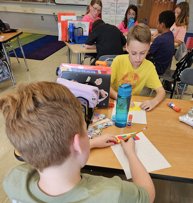 Two fourth-grade boys work at desks with multi-colored tiles, building a graph.