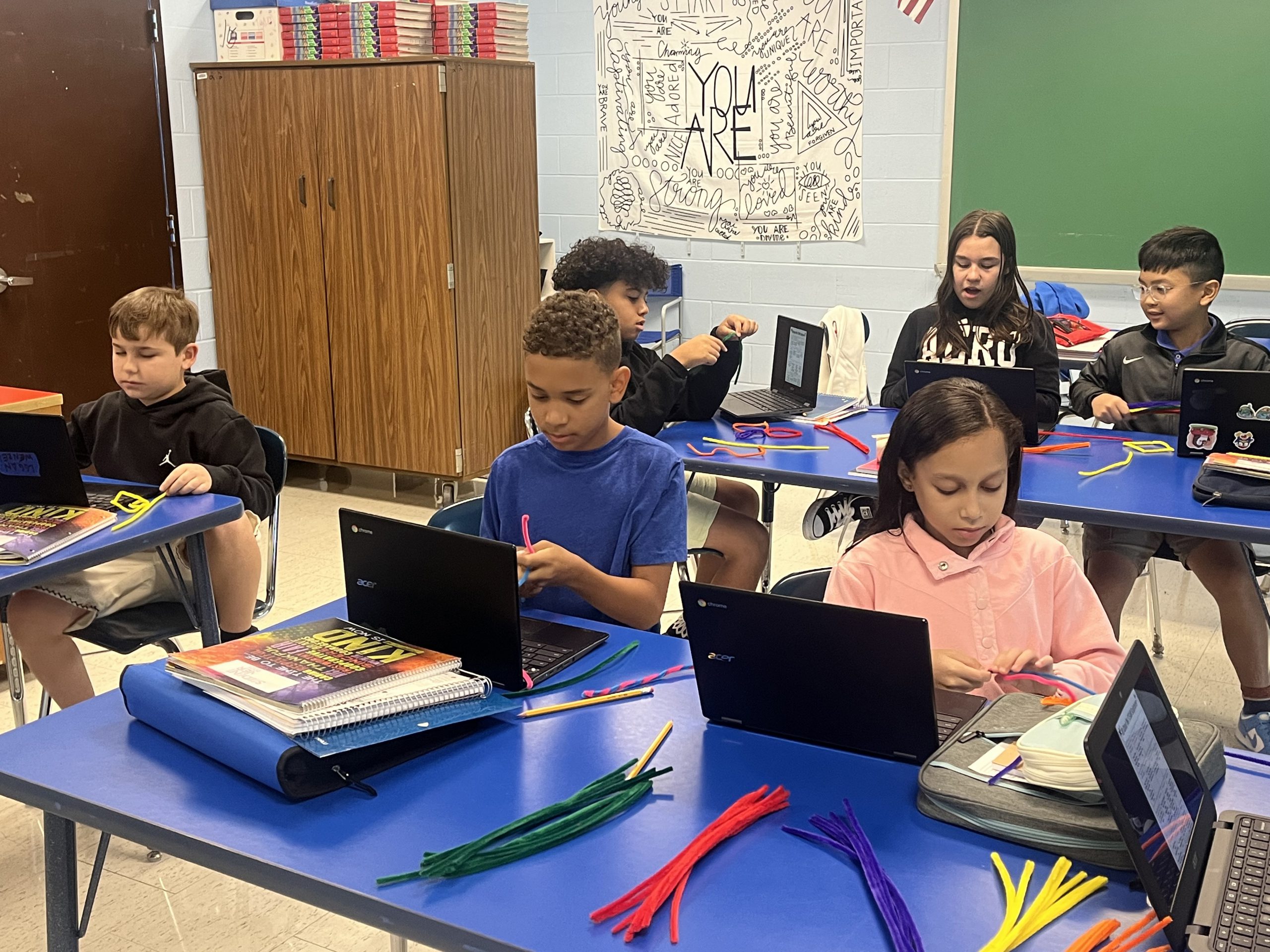 Six middle school kids sit in their classroom working on their chromebooks.