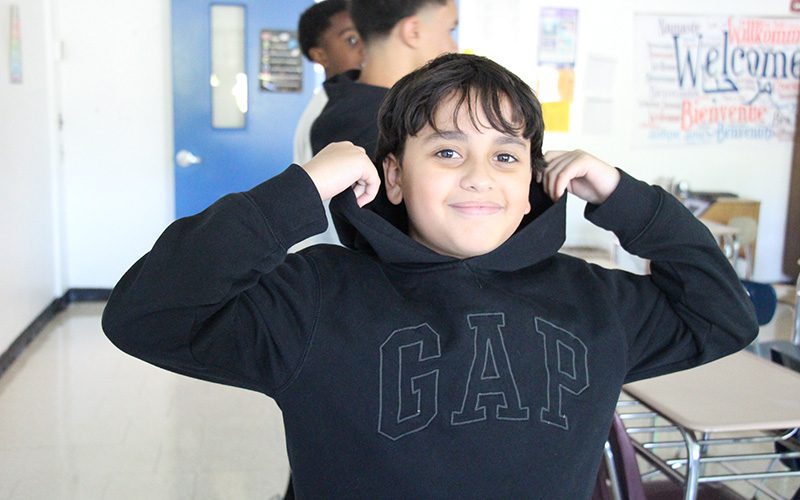 A middle school boy smiles. He is wearing a black hoodie.