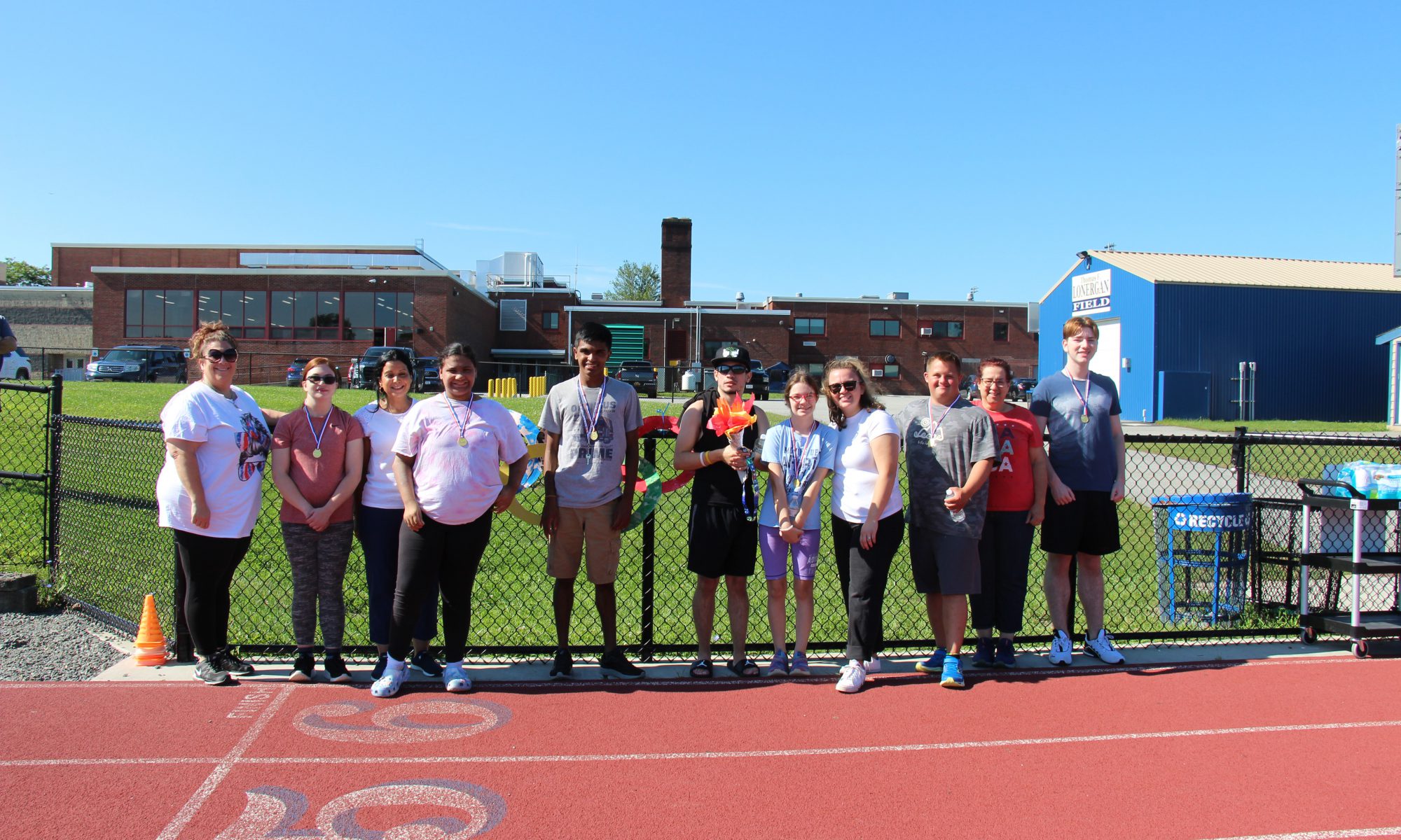 A group of seven high school students and four adults standing together in a line on an outdoor track.