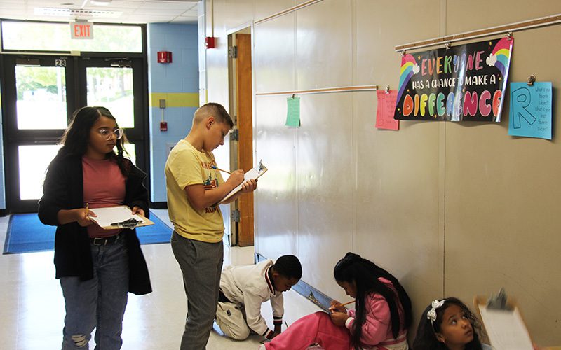 A group of fifth-grade students walk around with clipboards and pencils on a scavenger hunt.