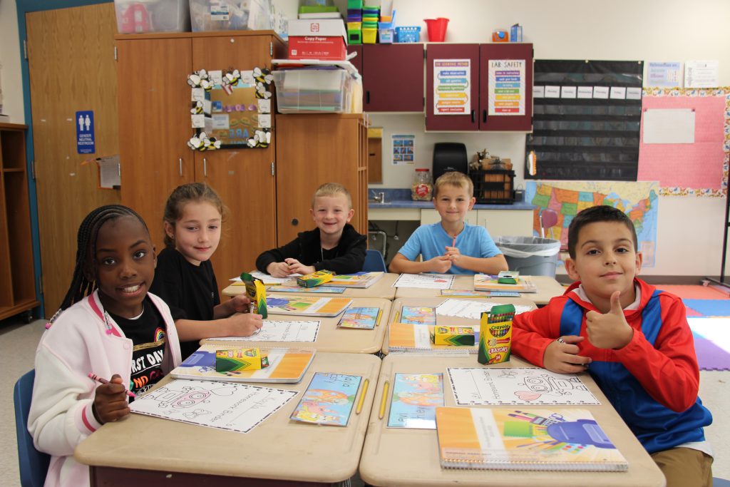 A group of younger elementary students sit at desks pushed together