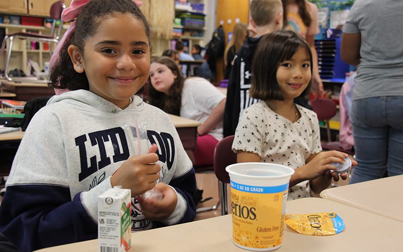 Two older elementary students sit at a table eating breakfast.