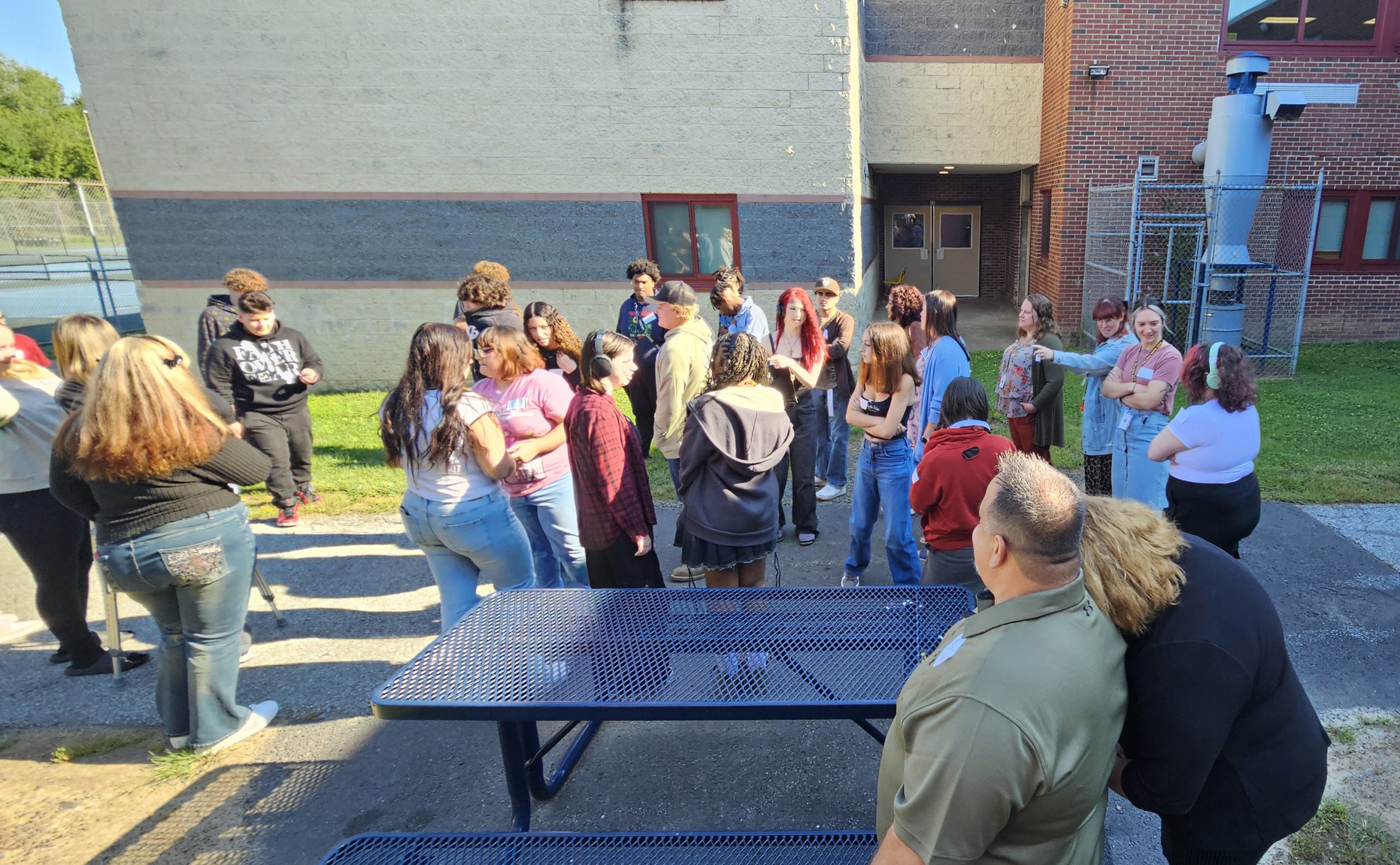 A group of high school students and adults hover around outdoors on a beautiful day.