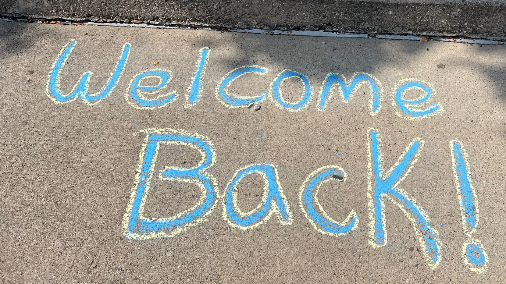 A sidewalk with Welcome Back written in blue and gold chalk.