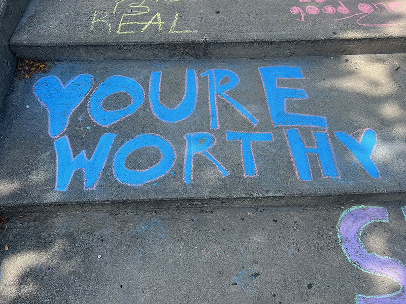 A concrete step with You're worthy written in blue chalk.