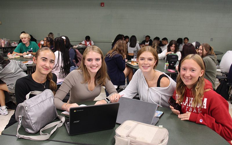 Four high school girls sit at a table and smile.