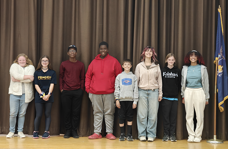 Eight middle school students stand on a stage smiling.