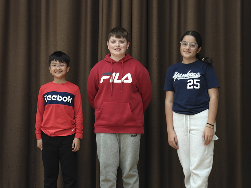 Three middle school students stand on a stage smiling.