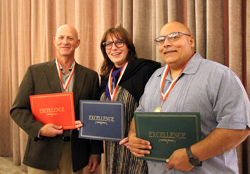 Two men and a woman stand together smiling. they are each holding a certificate and have medals around their necks on red white and blue ribbon.