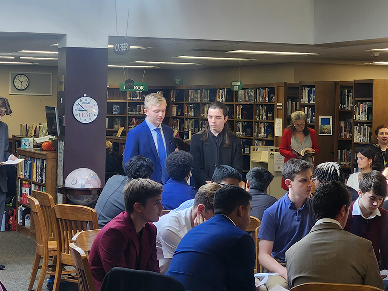 Students are seated  listening to adults talk.