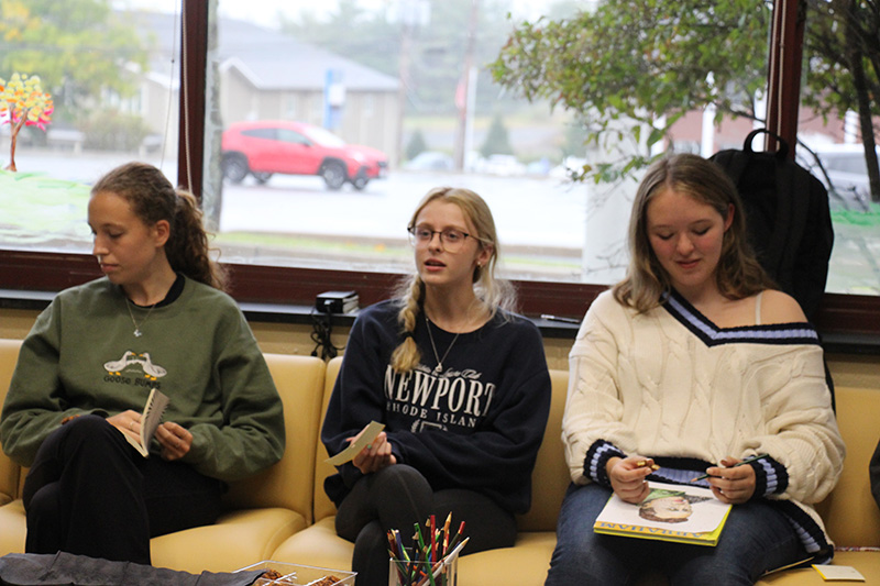 Three high school girls sit on a couch and talk.