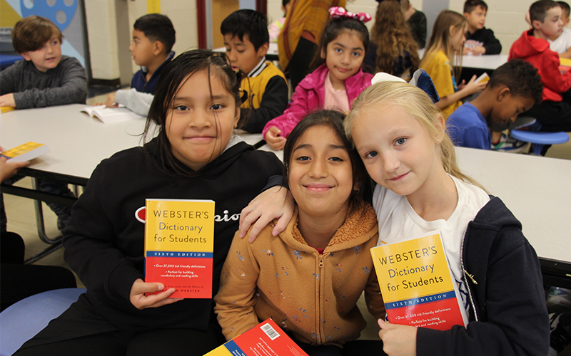 Three third-grade girls smiling as they hold up their new dictionaries.