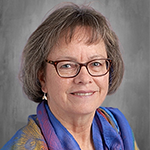 A woman with chin length darker hair and glasses, smiles.