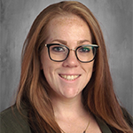 A woman with long reddish hair and glasses smiles.