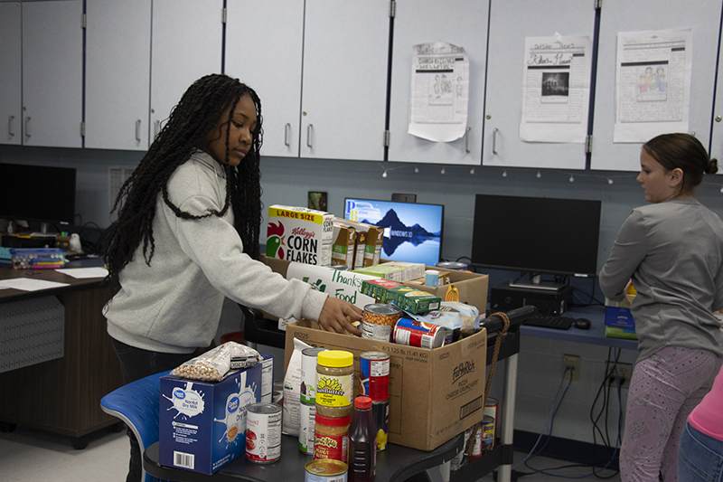 A middle school girl puts food on a cart. Another girl is standing next to her.