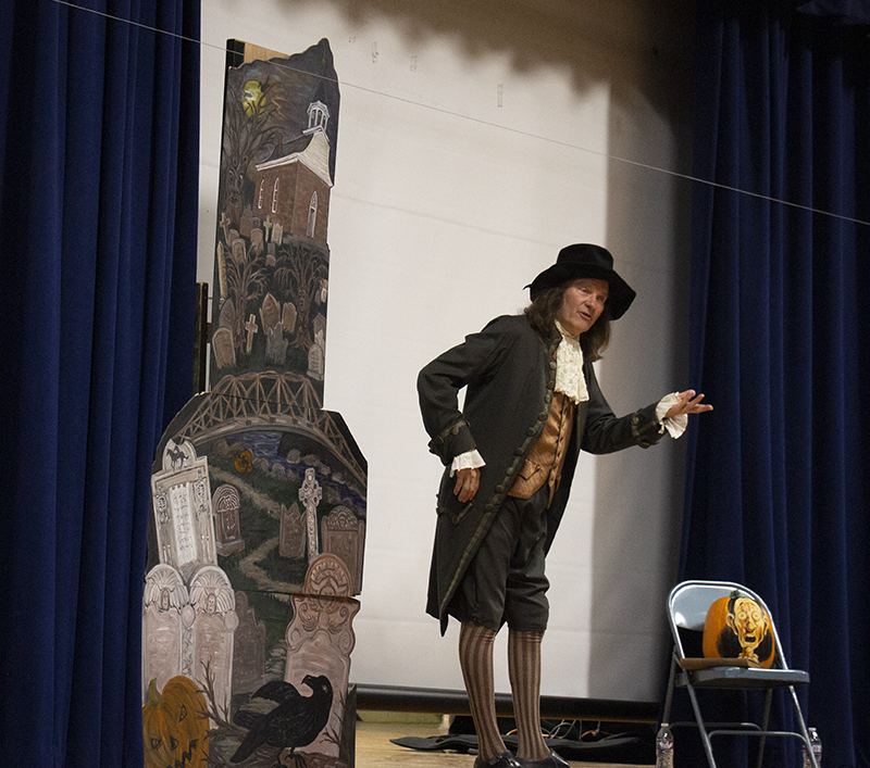 A man is on a stage dressed in period clothing while he performs the Legend of Sleepy Hollow.