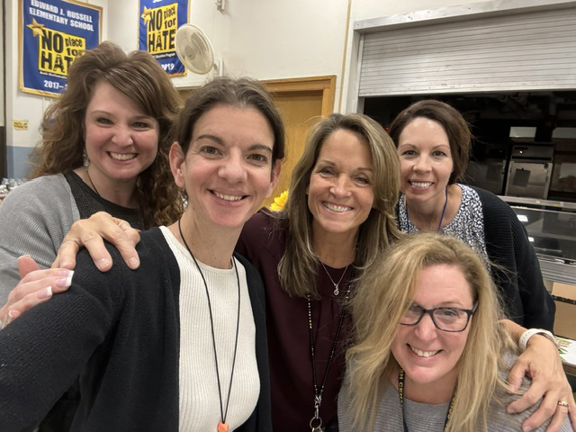 Five women stand together smiling.