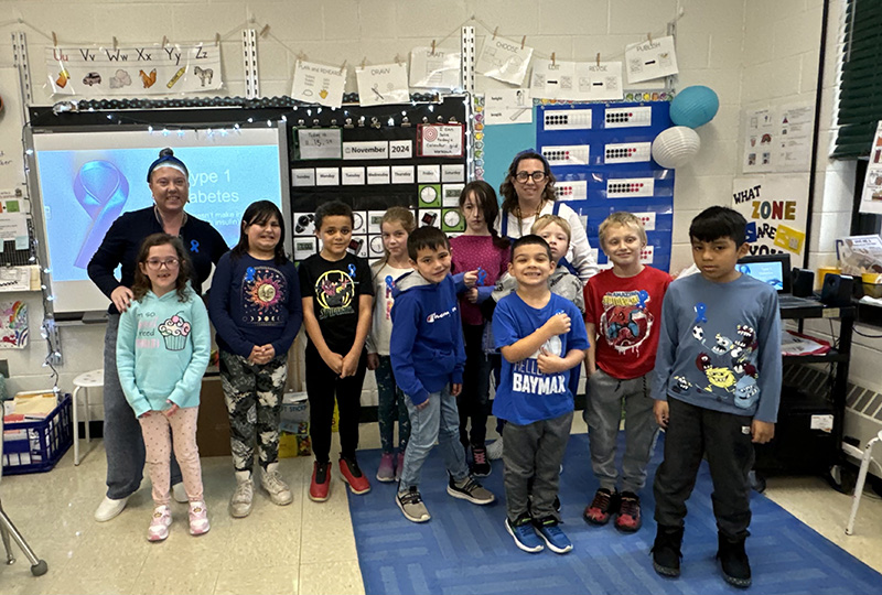 A group of elementary students stand with a couple of adults, all wearing blue for diabetes awareness.