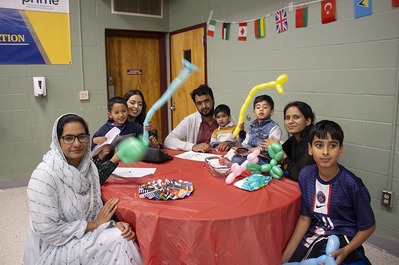 A family of four adults and four children sit around a table and smile. Some of the kids are holding balloon animals.