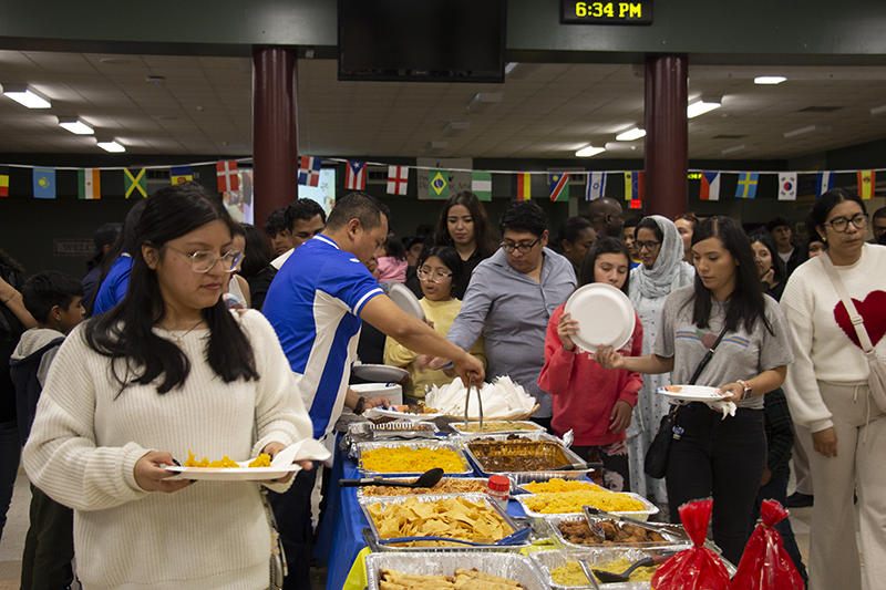 A long table filled with different foods. Many people take food onto their plates from both sides of the table.