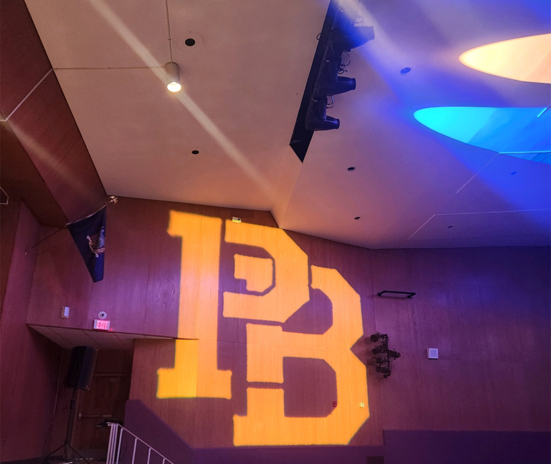 An auditorium wall with a big PB reflected on it.