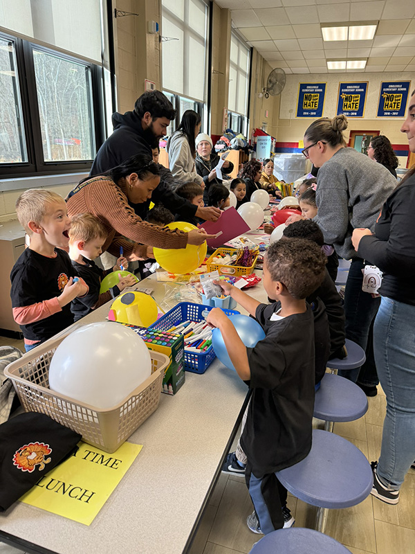 Many elementary school students kneel at a table to decorate balloons.