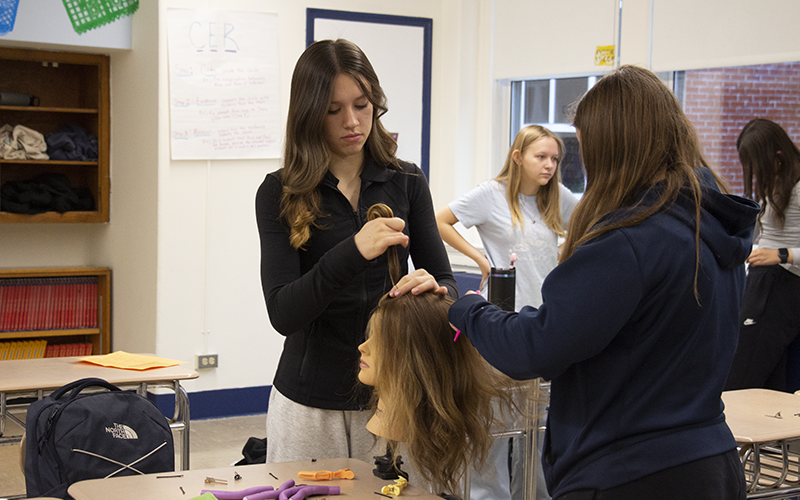 Middle school girls work on a mannequin head, fixing hair.