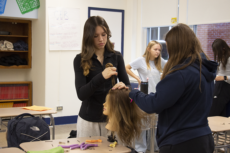 Middle school girls work on a mannequin head, fixing hair.