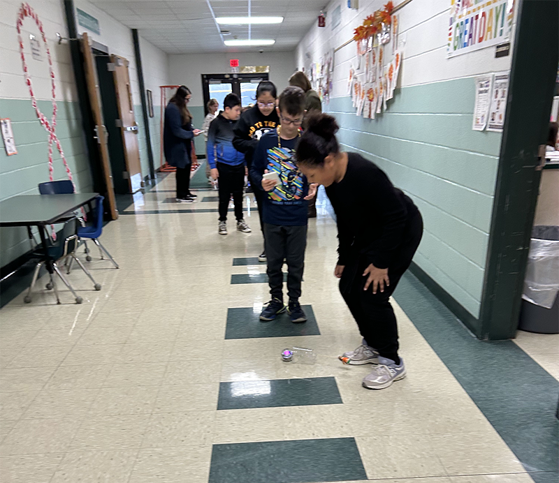 A girl looks closely at a little balloon made from clay that is riding on a little computerized ball down a hall.