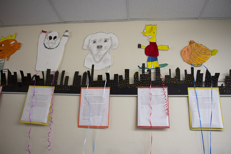 Students' typed letters are on a wall with a paper character they created above it.