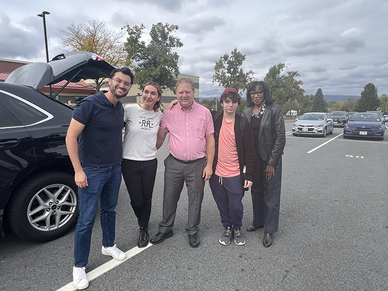 Five people stand together and smile in a parking lot.