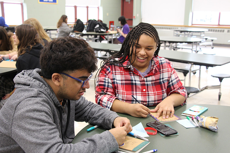 A high school boy and girl sit at a table writing in journals. 