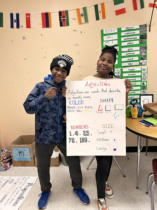 Two middle school students hold a poster that lists adjectives.