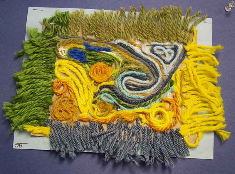 Many colored yarns are pasted onto a board in a swirly pattern