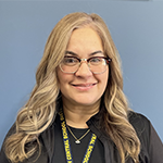 a woman smiles. She is wearing glasses and a black shirt. She has long blonde hair.