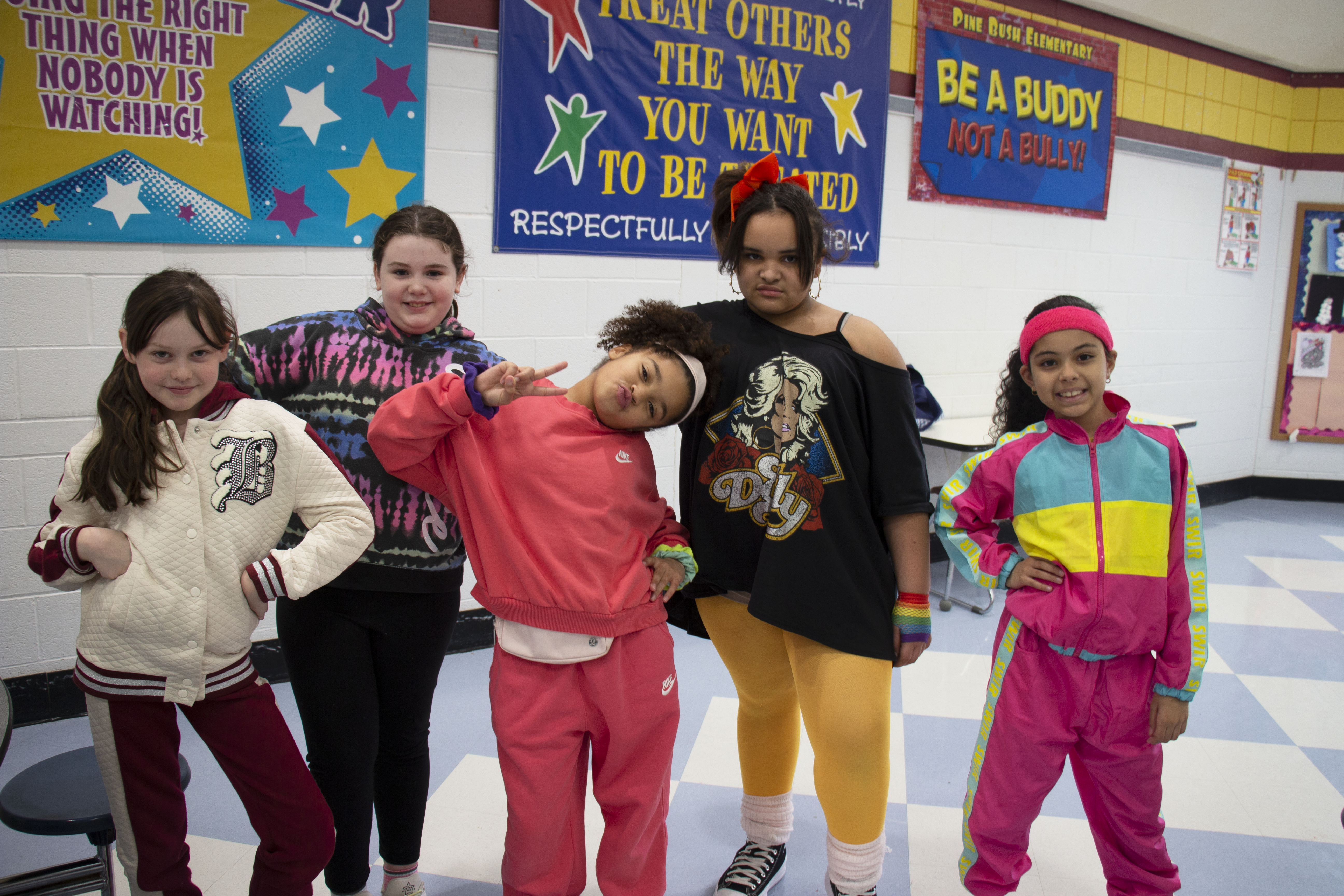 Five elementary girls wearing brightly colored 80s themed clothes. 