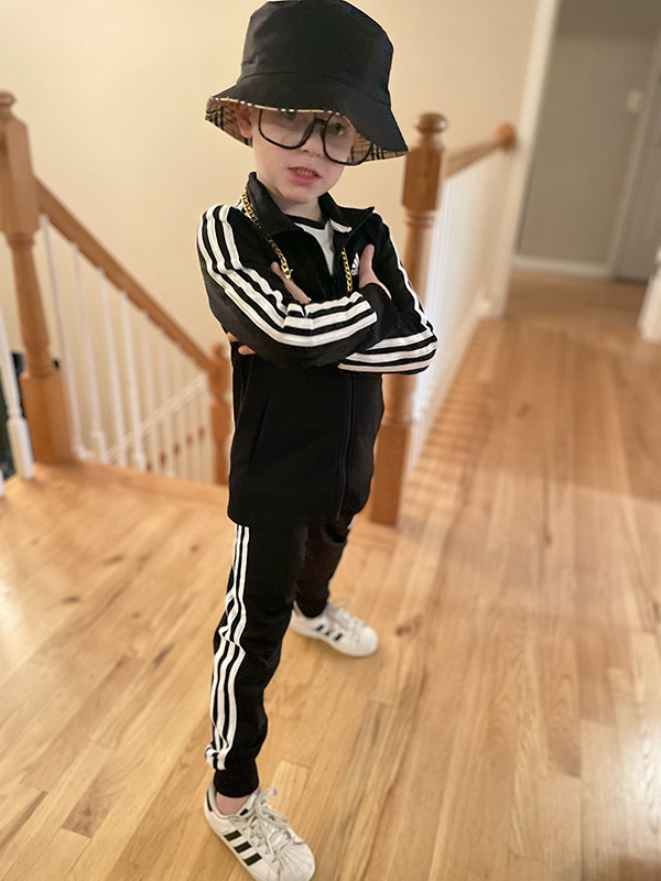 A boy wearing a black and white athletic suit with a black bucket hat. He has his arms crossed.