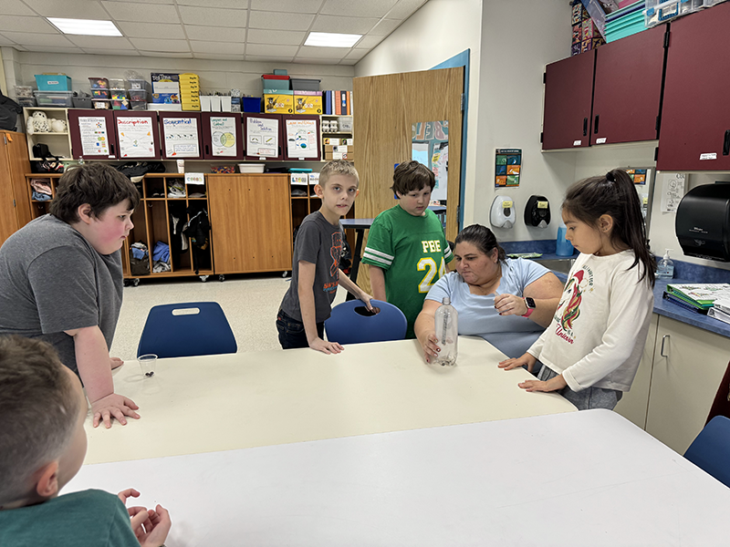 A group of elementary student work with an adult on an experiment.