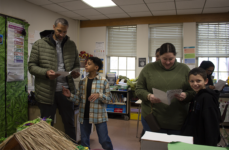 Two fourth-grade students stand with adults looking at their diorama projects.